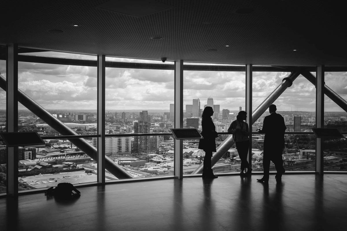Three colleagues talking beside floor-to-ceiling office windows overlooking a city