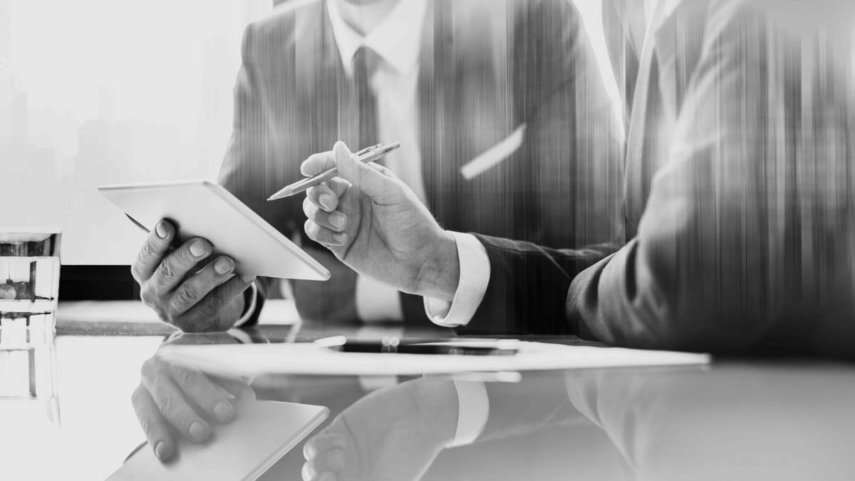 A director reviewing documents on a tablet with a pen at a boardroom table